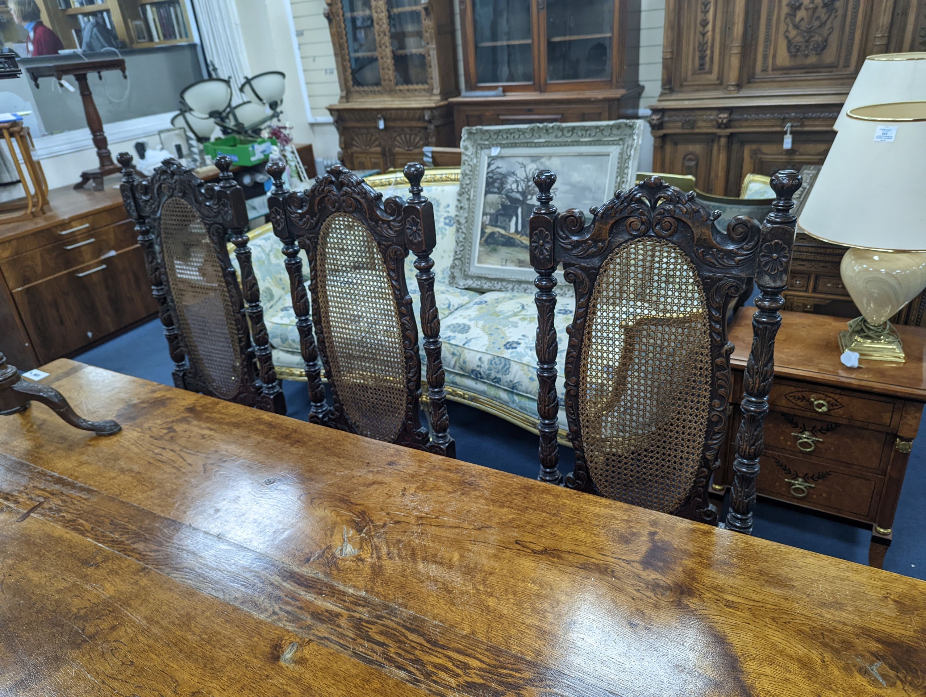 A set of six Charles II style carved oak dining chairs with caned backs and seats and squab cushion seats